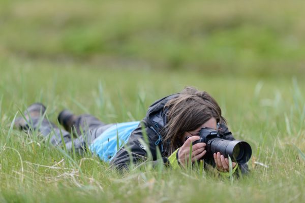 Sophie allongée dans l'herbe en train de prendre une photo, Hornstrandir Islande